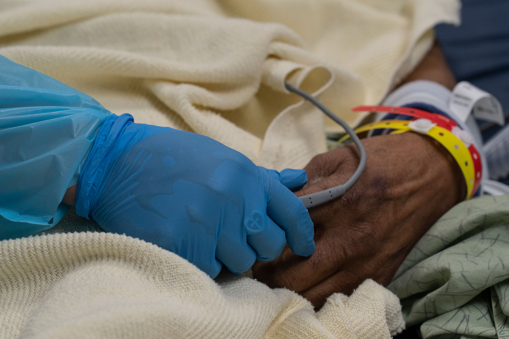 A medical staff member holds the hand of a patient admitted to the COVID-19 intensive care unit for treatment.