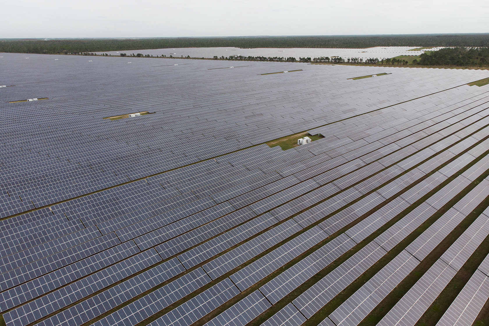 Photo shows rows of solar panels in a flat area with a body of water in the background