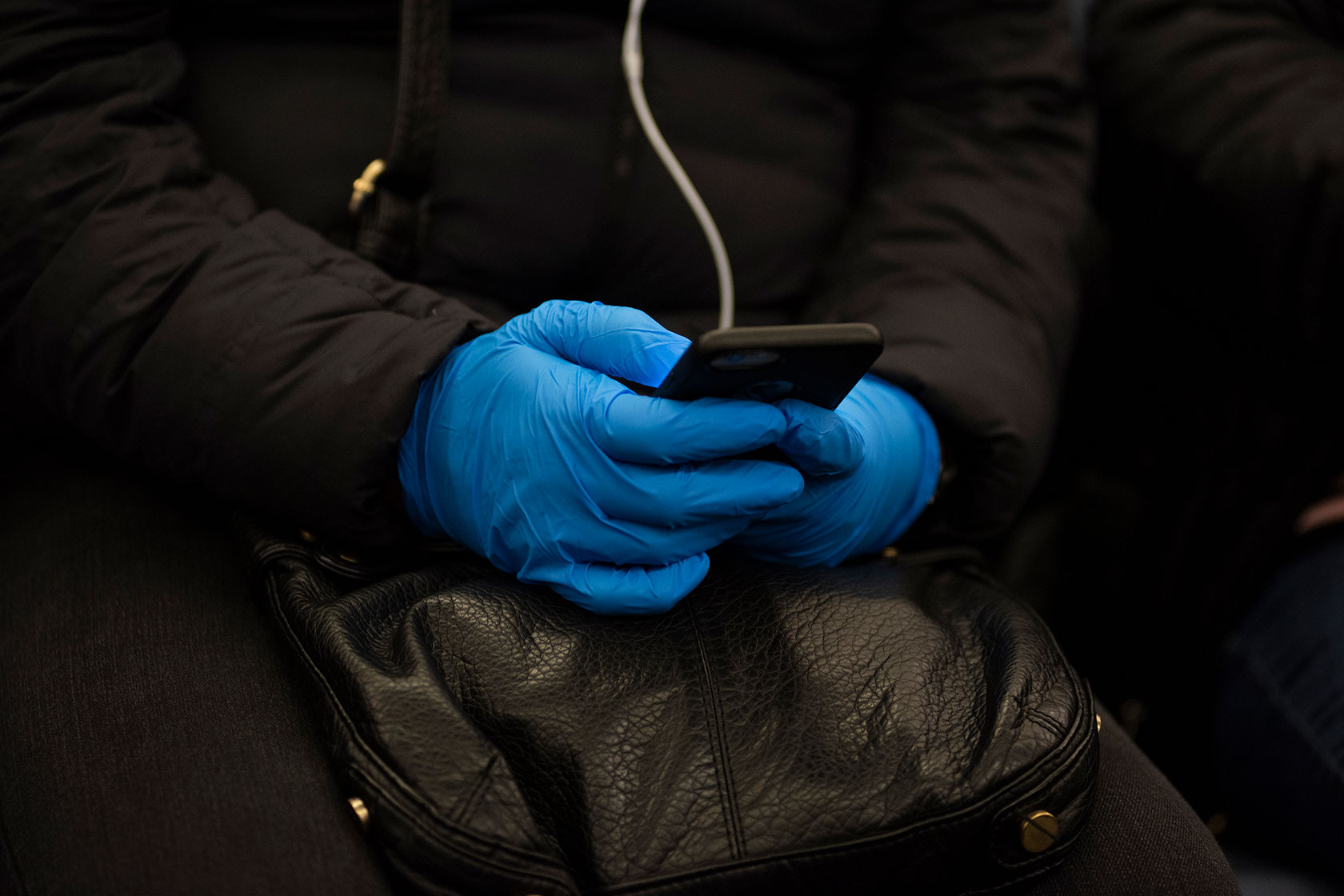 A subway train passenger uses their phone while wearing surgical gloves.