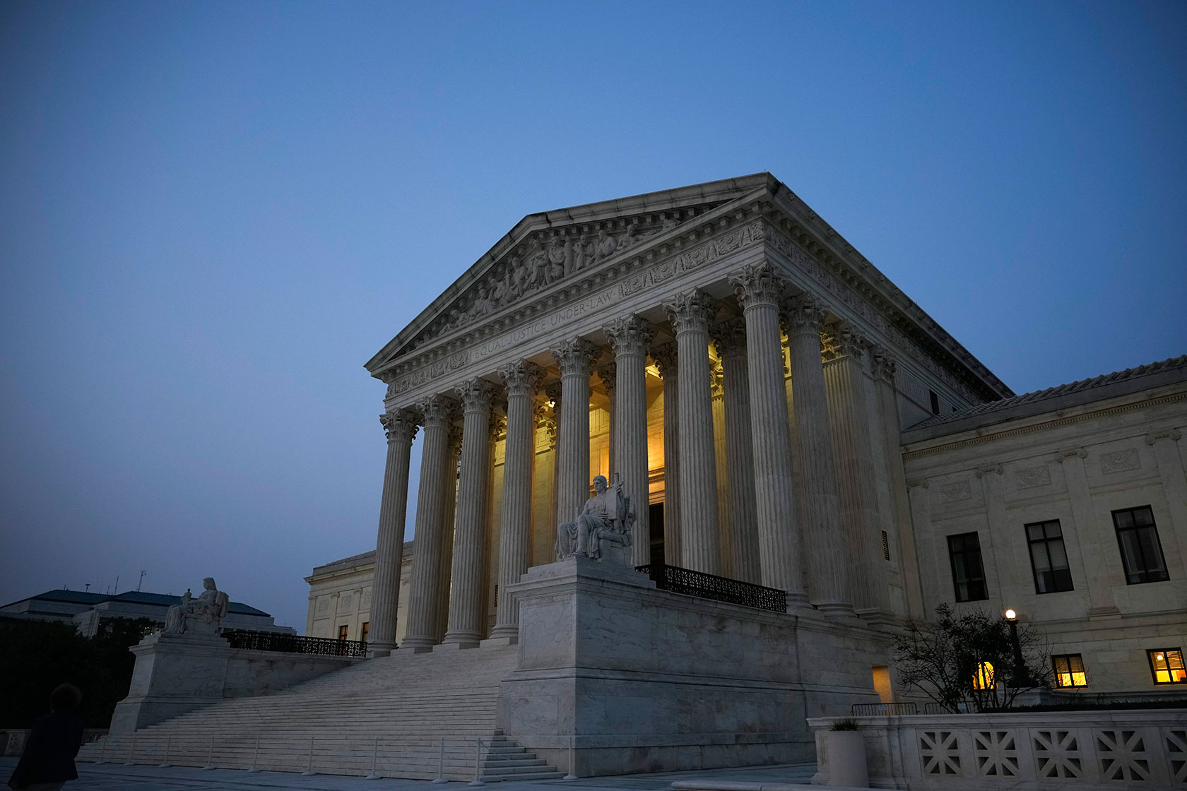 Photo shows a Supreme Court building partly lit inside, against a dark blue sky