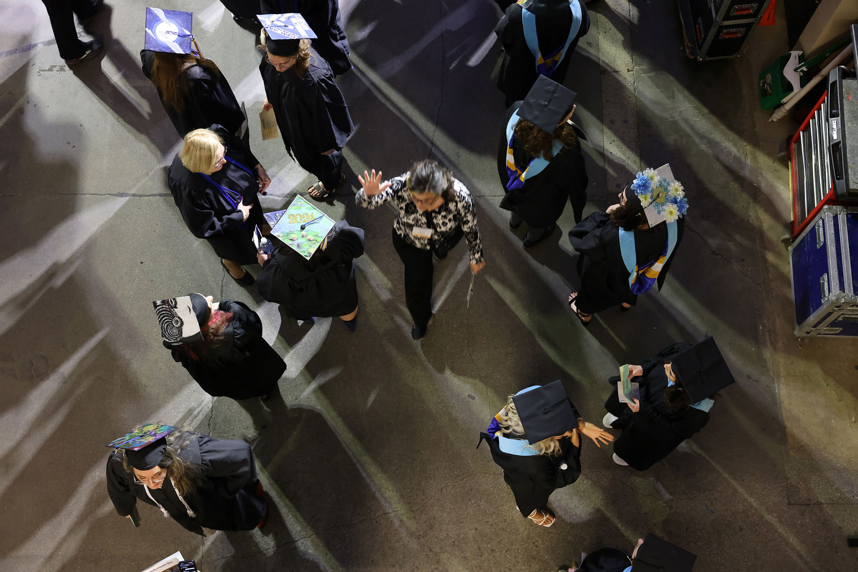 An aerial view of a volunteer with one hand raised walking through a cluster of students dressed in caps and gowns.