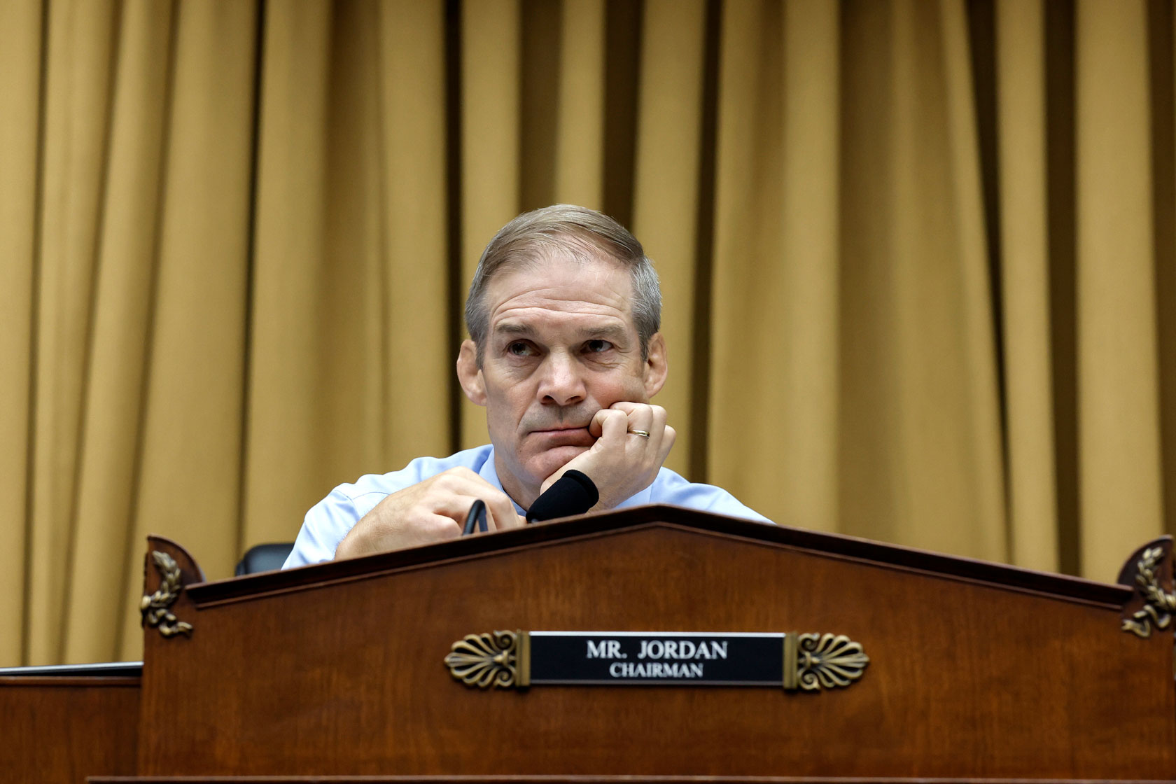 Rep. Jim Jordan is seen staring intently from behind a podium with one hand propping up his face.