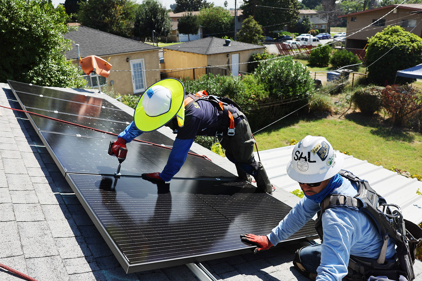 Photo shows two workers wearing protective gear installing a couple solar panels on a sunny rooftop