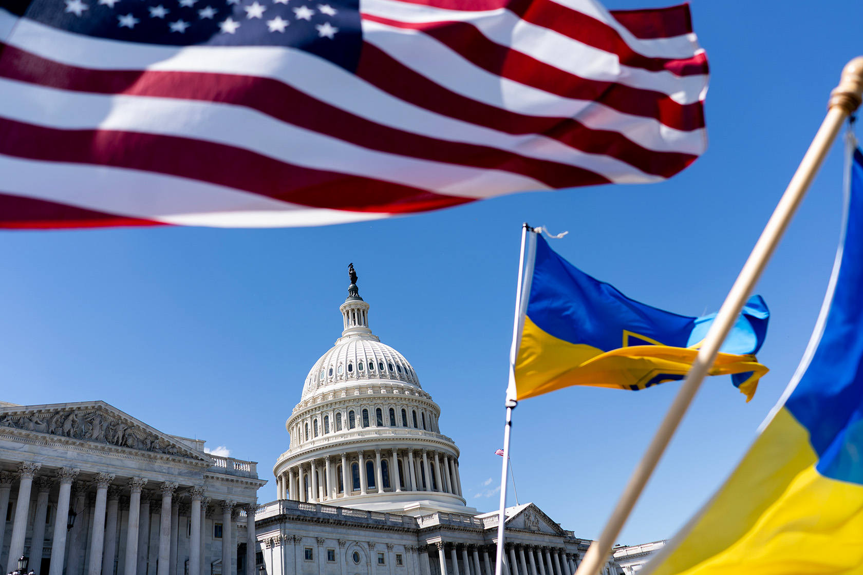 flags flying in front of the capitol building with a blue sky